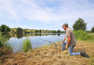 En mand fisker på bredden af en sø ved Huttopia Etang de Fouché, omgivet af natur i Bourgogne, Frankrig.