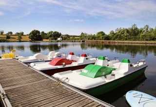 Pedal boats lined up at a wooden pier on the lake at Huttopia Etang de Fouché in Bourgogne-Franche-Comté, France.