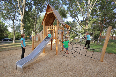Children play on a playground with a slide and climbing net at Huttopia Etang de Fouché in France.