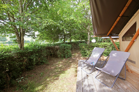 Holzterrasse mit zwei Liegestühlen vor einem Safarizelt bei Huttopia Etang de Fouché, Frankreich.