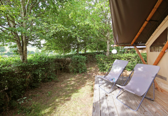 Holzterrasse mit zwei Liegestühlen vor einem Safarizelt bei Huttopia Etang de Fouché, Frankreich.