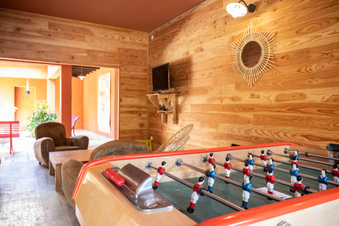 Sala de juegos con futbolín, sillones, televisor y paredes de madera en Huttopia Fontvieille, Provenza, Francia.