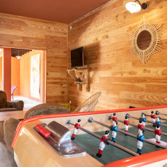 Sala de juegos con futbolín, sillones, televisor y paredes de madera en Huttopia Fontvieille, Provenza, Francia.