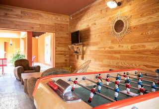 Sala giochi con calcio balilla, poltrone, TV e pareti in legno a Huttopia Fontvieille in Provenza, Francia.