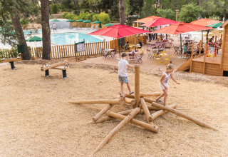 Kinderen spelen op houten speeltoestel bij zwembad en terras in Huttopia Fontvieille, Frankrijk.