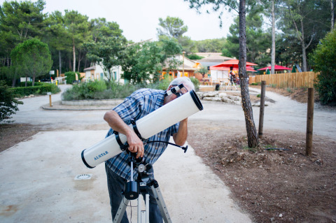 Un hombre con camisa a cuadros usa un telescopio en un parque de vacaciones arbolado en Provenza, Francia.