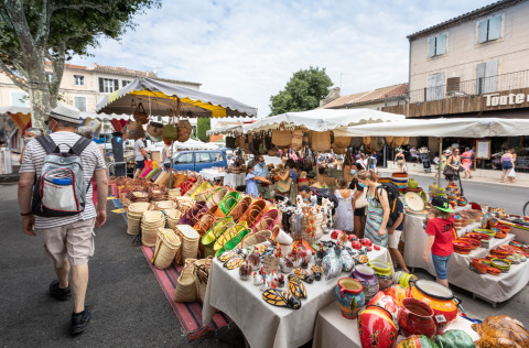 Outdoor market near Fontvieille, Provence, featuring colorful pottery and baskets at busy vendor stalls.