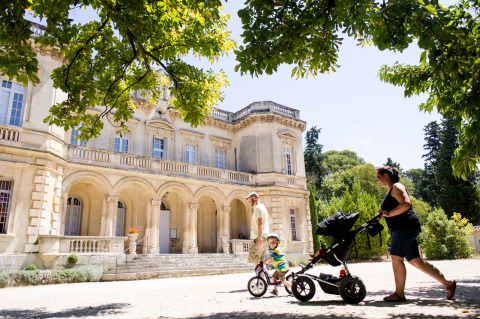 Gezin met kinderwagen en fiets passeert voor historisch gebouw te Fontvieille, Provence, Frankrijk.