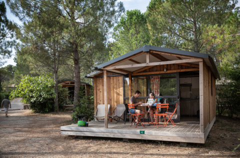 Gezin zit aan een tafel op de veranda van een houten lodge bij Chalet Evasion, omringd door dennen.