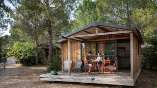 Gezin zit aan een tafel op de veranda van een houten lodge bij Chalet Evasion, omringd door dennen.
