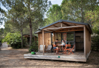 Gezin zit aan een tafel op de veranda van een houten lodge bij Chalet Evasion, omringd door dennen.
