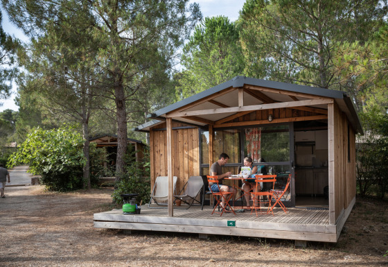 Gezin zit aan een tafel op de veranda van een houten lodge bij Chalet Evasion, omringd door dennen.