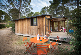Een kind speelt aan een oranje tafel voor een houten lodge bij Chalet Evasion, Huttopia Fontvieille, Frankrijk.