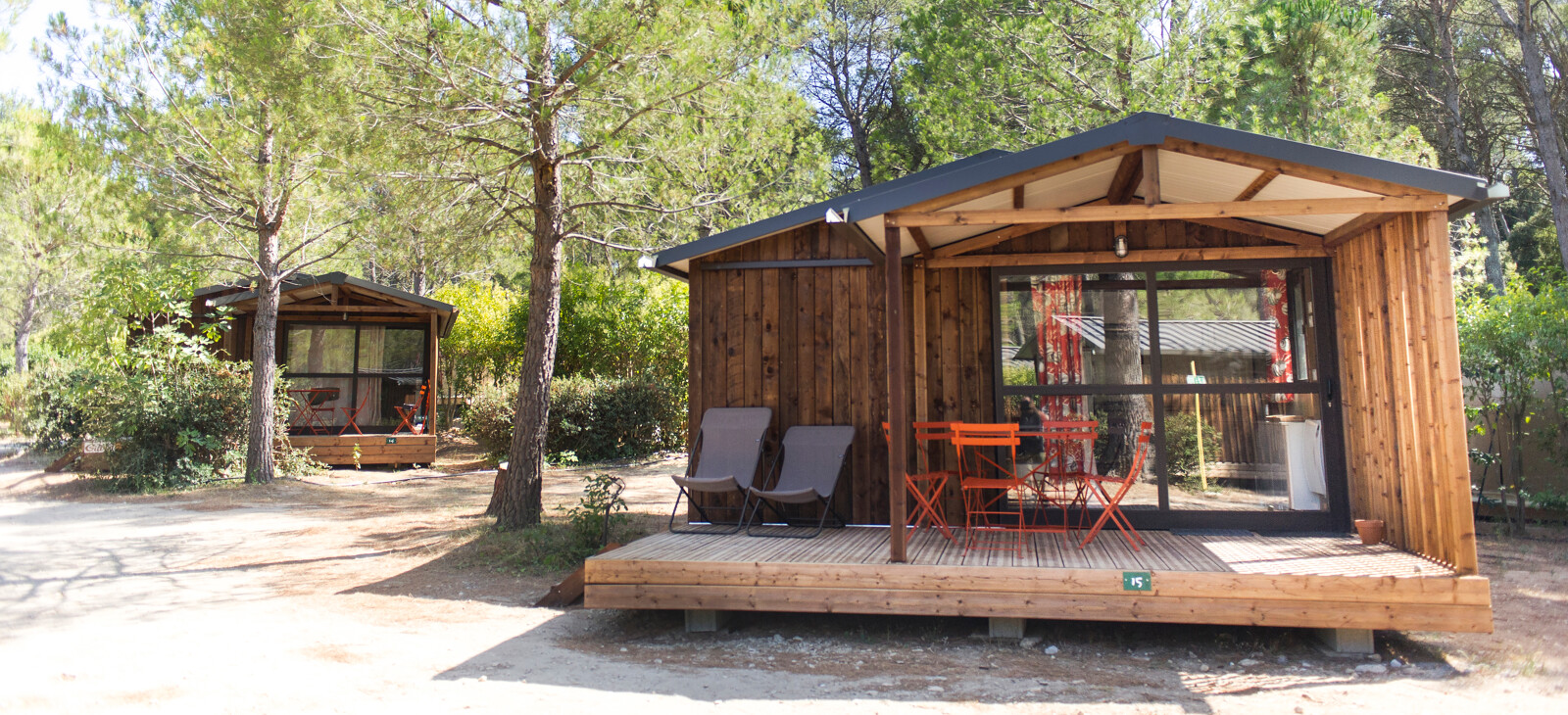 Twee houten lodges met terrassen en buitenmeubilair bij Chalet Evasion, Huttopia Fontvieille in Frankrijk.