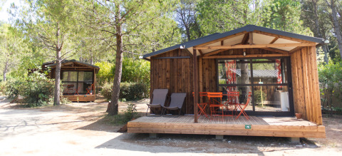 Twee houten lodges met terrassen en buitenmeubilair bij Chalet Evasion, Huttopia Fontvieille in Frankrijk.