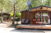Twee houten chalets met terras en tuinmeubels bij Chalet Evasion, Huttopia Fontvieille in Frankrijk.