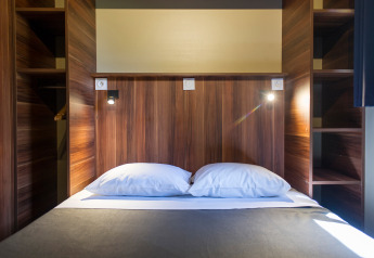 Modern tweepersoonsbed in een houten glamping-chalet met ingebouwde planken en leeslampjes aan beide zijden.