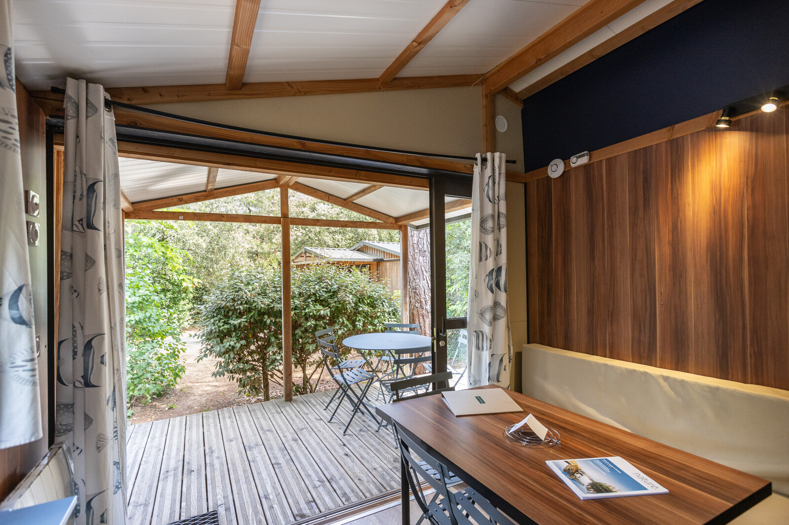 Binnenaanzicht van Chalet Evasion glamping met tafel, stoelen en overdekt terras tussen het groen.