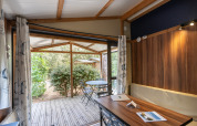 Vista interior del glamping Chalet Evasion con mesa, sillas y terraza cubierta rodeada de vegetación.