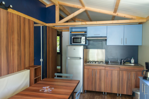 Indretning af Chalet Evasion glampingkøkken med træskabe, spisebord, køleskab og komfur under loftsbjælker.