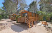 Cabañas de madera en un bosque, Roulotte en Huttopia Fontvieille Francia, con porche y mesa de picnic.