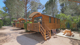 Roulotte en bois dans un cadre forestier, Huttopia Fontvieille en France, avec terrasse et table de pique-nique.