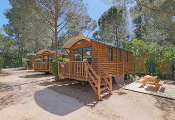 Roulotte en bois dans un cadre forestier, Huttopia Fontvieille en France, avec terrasse et table de pique-nique.