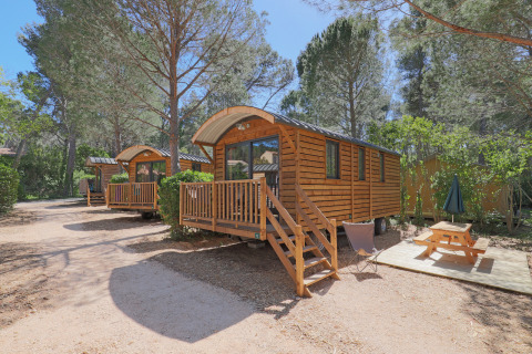 Cabañas de madera en un bosque, Roulotte en Huttopia Fontvieille Francia, con porche y mesa de picnic.