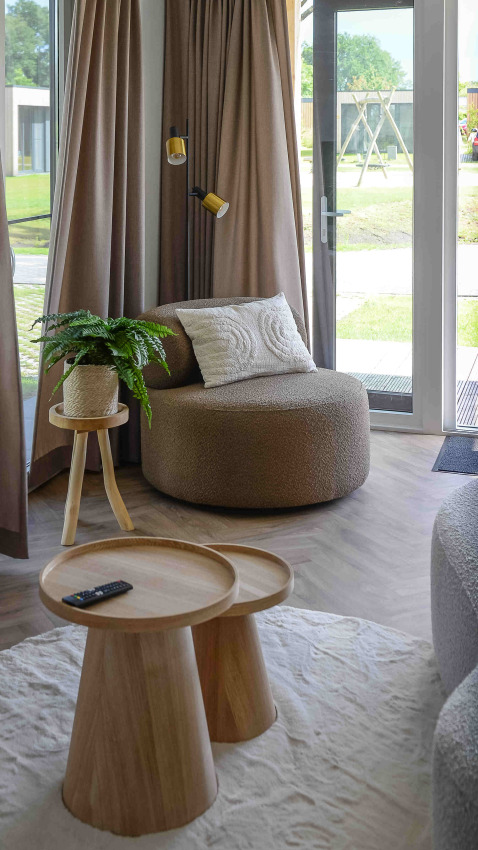 Sala acogedora en Panorama Wellness Lodge con sillón redondo, mesas de madera y vista al jardín.