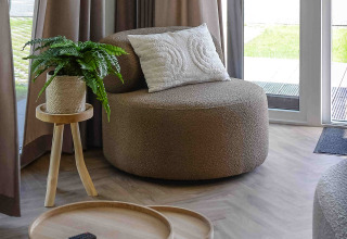 Sala acogedora en Panorama Wellness Lodge con sillón redondo, mesas de madera y vista al jardín.