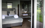 Moderne lodge med dobbeltseng og åbent badeværelse, store vinduer og udsigt til grøn natur i Holland.