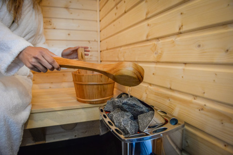 Persona in accappatoio versa acqua sulle pietre calde della sauna al Panorama Wellness Lodge, Vakantiepark Hölte.