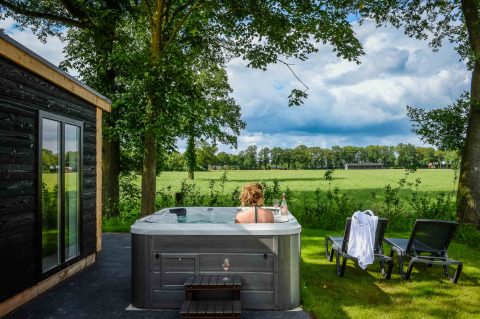 Kvinde slapper af i udendørs jacuzzi ved Panorama Wellness Lodge med udsigt over grønne marker i Nederlandene.