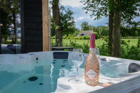 Sprudelnder Whirlpool mit Prosecco und Gläsern im Panorama Wellness Lodge, Vakantiepark Hölte, Niederlande.