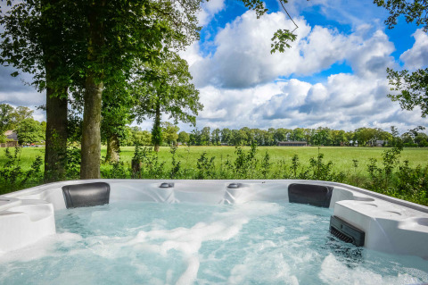 Jacuzzi all'aperto con vista su campi verdi e alberi al Panorama Wellness Lodge nei Paesi Bassi.