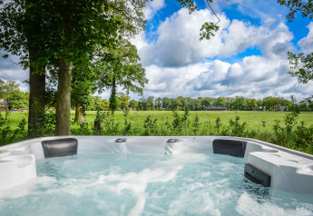 Jacuzzi all'aperto con vista su campi verdi e alberi al Panorama Wellness Lodge nei Paesi Bassi.
