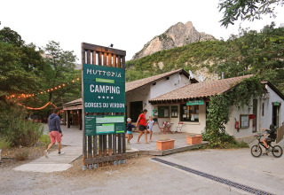 Indgang til Huttopia Gorges du Verdon campingplads med gæster og bjergrigt landskab i baggrunden.