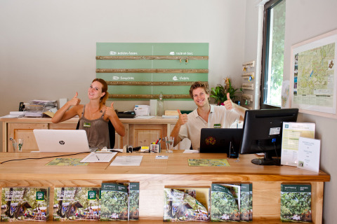 Receptionists giving thumbs up and smiling at the front desk of Huttopia Gorges du Verdon holiday park, France.