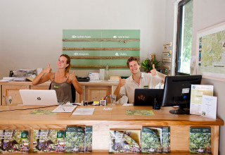 Receptionists giving thumbs up and smiling at the front desk of Huttopia Gorges du Verdon holiday park, France.