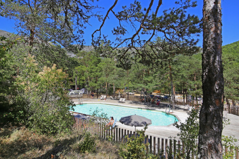 Vista de una piscina al aire libre rodeada de árboles en el parque vacacional Huttopia Gorges du Verdon, Hauts-de-France.