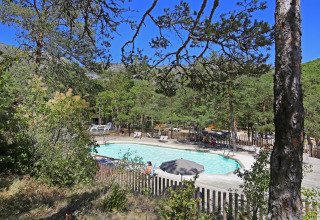 Udsigt over en udendørs swimmingpool omgivet af træer i ferieparken Huttopia Gorges du Verdon, Hauts-de-France.