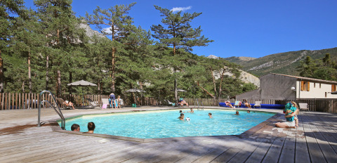 Piscina al aire libre rodeada de pinos y montañas en el parque vacacional Huttopia Gorges du Verdon, Francia.