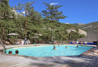 Udendørs swimmingpool omgivet af fyrretræer og bjerge på Huttopia Gorges du Verdon feriepark i Frankrig.
