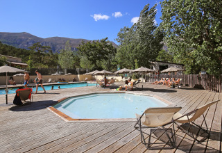 Feriegæster slapper af ved swimmingpoolen i Huttopia Gorges du Verdon, omgivet af bjerge og træer.