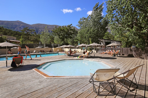 Vacanciers se détendent près de la piscine à Huttopia Gorges du Verdon, paysage de montagnes en arrière-plan.