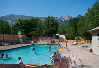 Børn og voksne nyder poolområdet med liggestole og bjerge i baggrunden på Huttopia Gorges du Verdon.