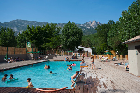 Families swim and relax by a pool with mountain scenery at Huttopia Gorges du Verdon holiday park, France.