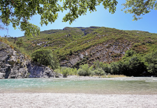 Flod med klart vand og grønne bjerge under blå himmel ved Huttopia Gorges du Verdon i Hauts-de-France.