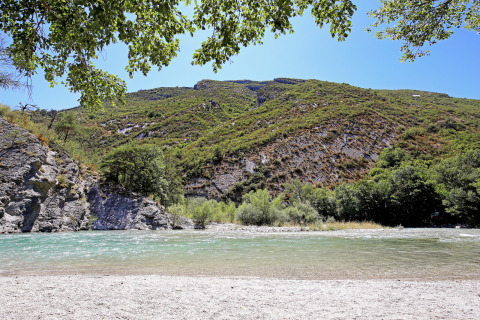 Rivière à l’eau claire et collines verdoyantes à Huttopia Gorges du Verdon, Hauts-de-France sous ciel bleu.