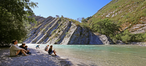 Familias disfrutan junto al río con formaciones rocosas inclinadas en Huttopia Gorges du Verdon, Francia.